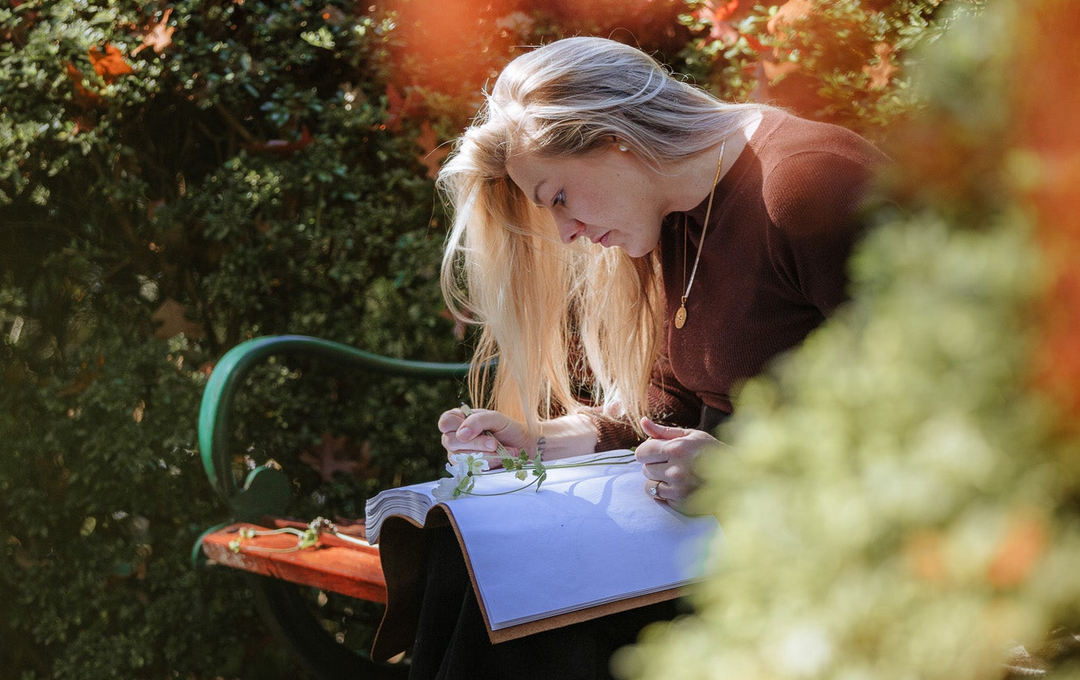 Steph sitting on a garden bench sketching