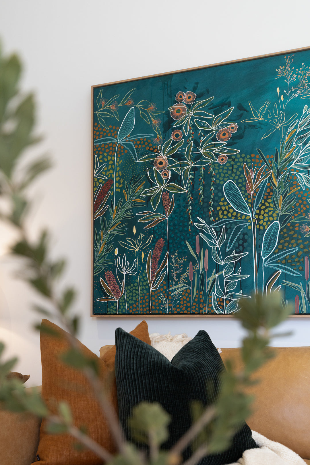 Framed botanical artwork on a wall with a couch and pillows in the foreground.